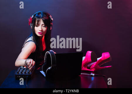 Junge DJ-Frau gekleidet in rosa Schuhe liebt Musik. Glamouröse Mädchen mit headphne auf rotem und blauem Hintergrund spielt Musik Disko. Stockfoto