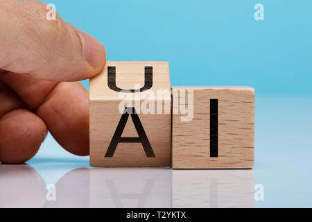 Person's Hand Holzblock mit UI und AI Text über der reflektierenden Hintergrund Stockfoto