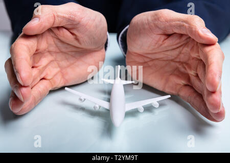 Nahaufnahme der Hand schützen das Flugzeug auf weißem Schreibtisch Stockfoto