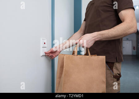 Delivery Man Läuten der Türklingel mit einer braunen Papiertüte In Der Hand Stockfoto