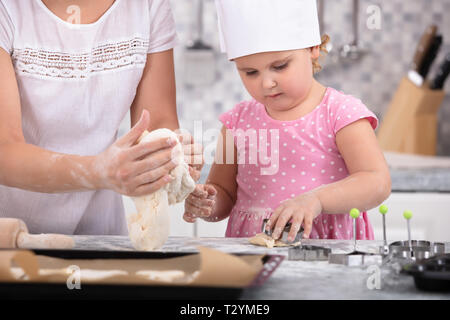 Mädchen mit Küchenchef hat zu helfen, ihre Mutter zu Cookies an Küche Stockfoto