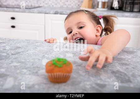 Lächelnd Cute Girl's Hand erreichen Für Cupcake auf den Küchentisch Stockfoto