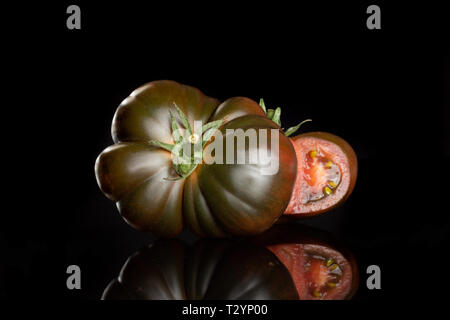 Eine ganze Hälfte des Fleischigen frische Tomaten primora auf schwarzem Glas isoliert Stockfoto