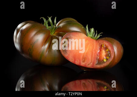Gruppe von einer ganzen Hälfte der frischen Tomate primora auf schwarzem Glas isoliert Stockfoto