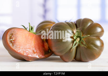 Eine ganze Hälfte des Dunklen frische Tomaten primora mit blauen Fenster in eine weiße Küche Stockfoto