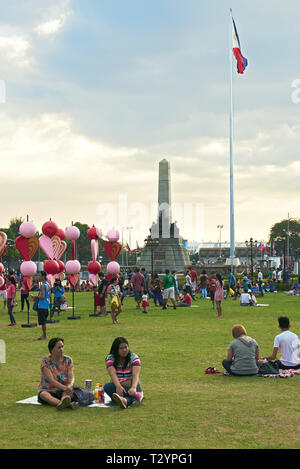 Manila, Philippinen: Festliche Szene mit Personen im Luneta Park mit dem Rizal Monument und der philippinischen Flagge im Hintergrund Stockfoto