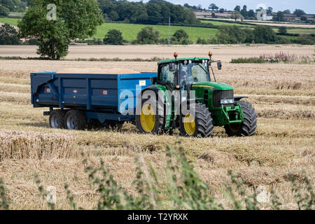 John Deere Traktor Ziehen eines Anhängers in einem Weizenfeld in der Erntezeit in North Yorkshire Stockfoto