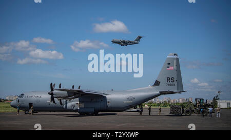 Ein US Air Force C-17 bis 16 Airlift Wing, Joint Base Charleston, Charleston, South Carolina zugewiesen wurde, werden im endanflug als US Air Force C-130J Hercules zugeordnet zu der 75th Expeditionary Airlift Squadron, Combined Joint Task Force-Horn von Afrika (CJTF-HOA) geladen wird mit Hilfe von der United Nations International Children's Emergency Fund (UNICEF), am Flughafen in Maputo, Mosambik, April 4, 2019. Die Task Force wird helfen, die Anforderungen von USAID assessment Teams und der humanitären Organisationen in der Region durch Bereitstellung von Logistik und Personal für die USA arbeiten identifiziert Stockfoto