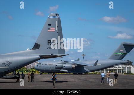 Ein US Air Force C-17 bis 16 Airlift Wing, Joint Base Charleston, Charleston, South Carolina zugeordnet, Taxis in Position als US Air Force C-130J Hercules zugeordnet zu der 75th Expeditionary Airlift Squadron, Combined Joint Task Force-Horn von Afrika (CJTF-HOA) geladen wird mit Hilfe von der United Nations International Children's Emergency Fund (UNICEF), am Flughafen in Maputo, Mosambik, April 4, 2019. Die Task Force wird helfen, die Anforderungen von USAID assessment Teams und der humanitären Organisationen in der Region durch Bereitstellung von Logistik und Personal für die USA arbeiten identifiziert Stockfoto