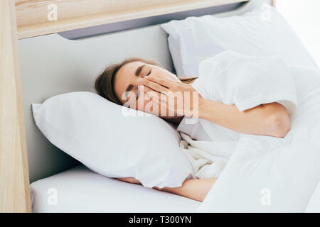 Sleepy kaukasischen Frauen mit geschlossenen Augen, den Mund mit der Hand und Gähnen beim Liegen auf dem bequemen Bett im Morgen Stockfoto