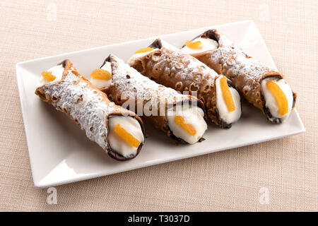 Vier frittierte cannoli Sicilia Gebäck mit Cremigem ricotta Füllung garniert mit Orangenschale und auf einer rechteckigen Platte serviert. Stockfoto