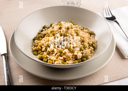 Schüssel mit traditionellen Risi e Bisi aus dem Veneto, Italien mit Lager, Reis, Gewürze und frische grüne Erbsen, am Tisch mit Geschirr serviert. Stockfoto