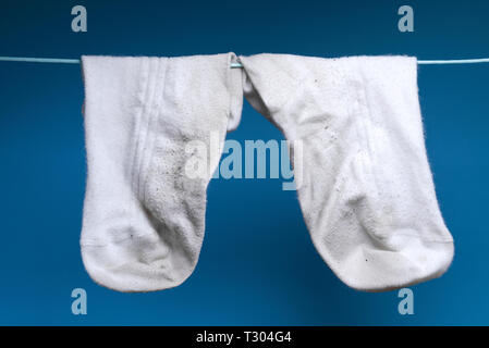 Zwei schmutzig weiß alte Socke wiegen auf dem Seil. blauen Hintergrund. Konzept der Wäsche, Reinigung Stockfoto