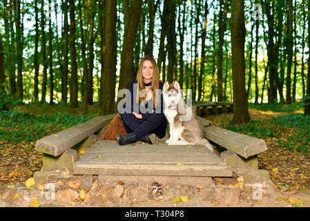 Junges Mädchen sitzt auf hölzerne Brücke in den Wald. weiter Puppy dog redhead Husky Stockfoto