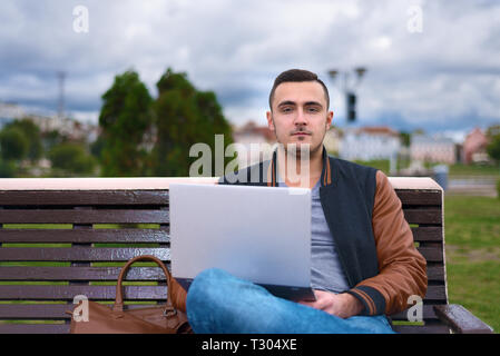 Porträt der jungen Kerl. Freelancer Arbeiten am Laptop in der Straße. Man sitzt auf der Bank Stockfoto