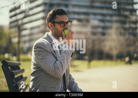 Junge Unternehmer ist Essen Apple im Park nach der Arbeit. Stockfoto