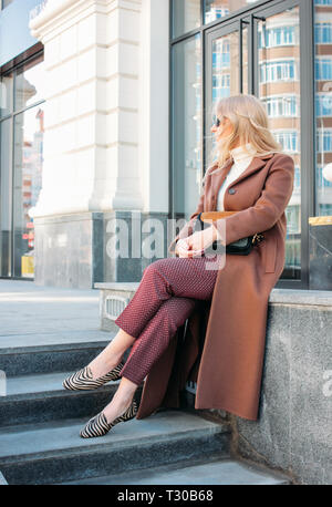 Elegante modische blonde Frau mit Mantel und Sonnenbrille, street style Foto Stockfoto