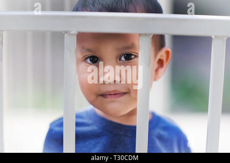 Junge Hispanic junge hinter Gittern aus einer Krippe traurig über das Erhalten einer Zeit heraus für schlechtes Verhalten. Stockfoto
