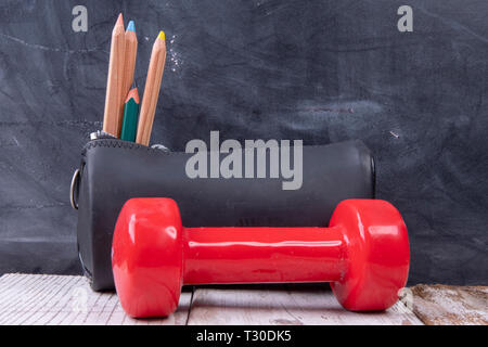 Hantel mit Bleistift und Buntstifte Holz vor einer Tafel - stark für Schule Stockfoto