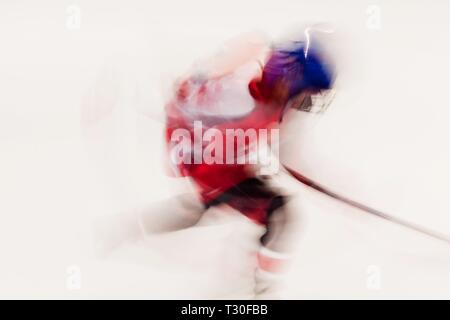 Hockey Player im roten Kleid und blauen Helm in Bewegung, verschwommene Bewegung auf dem Eis Stadion Stockfoto