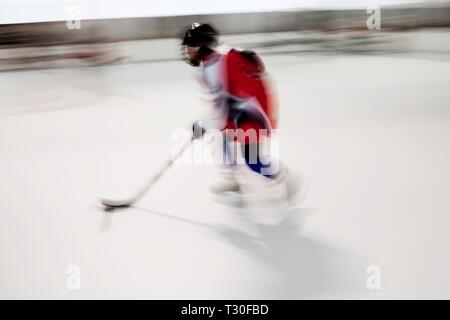 Jungen Hockeyspieler im roten Kleid und schwarzen Helm in Bewegung, verschwommene Bewegung auf dem Eis Stadion Stockfoto