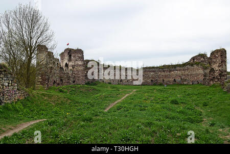 Die Ruinen einer alten Burg stand in einem Feld, auf denen wächst Frühling Gras und Blumen vor blauem Himmel Stockfoto