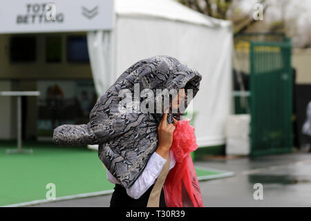 Frau, die sich bei starkem Regen unter einem Mantel in Aintree, Liverpool, 5.. April 2019, unterstellt. Wetter in Großbritannien. Starke Windböen, Regen, starke Regenschauer für den 2.-tägigen Grand National Horse Racing Festival. Stockfoto