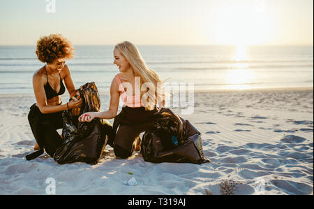 Zwei weibliche Freiwillige Müll sammeln vom Strand. Weibliche Surfer mit Müllsäcken Reinigung sandigen Küste. Stockfoto