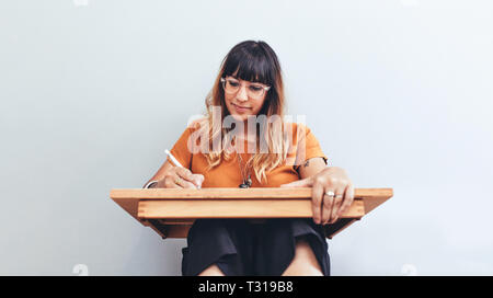 Porträt einer Frau sitzt auf dem Boden mit einer Zeichnung Pad eine Skizze. Nahaufnahme eines kreativen Künstler bei der Arbeit Erstellung einer Skizze. Stockfoto