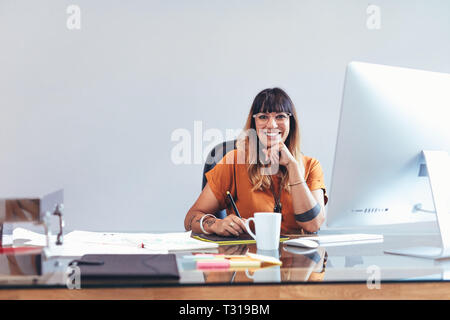 Lächelnde kreative Künstlerin an Ihrem Schreibtisch im Büro eine Skizze auf einem digitalen Schreibblock. Illustrator im Büro arbeiten an ihren Entwürfen o Stockfoto