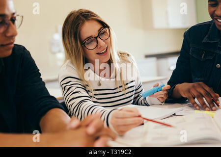 Studenten in Zusammenarbeit mit ihrer Zuordnung zur Bibliothek. Gruppe junger Leute sitzen am Tisch, die Bücher zu lesen. Stockfoto