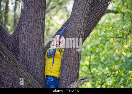 Der Junge im Wald zielt auf die Kamera mit einem Bogen Stockfoto