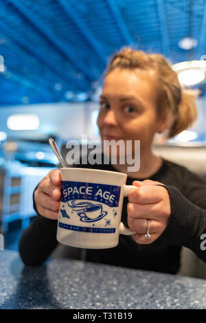 Gila Bend, Arizona - März 24, 2018: Junge Frau im Space Age Restaurant sitzen hält eine Tasse Kaffee. Frau ist absichtlich unscharf zu Schwerpunkte Stockfoto