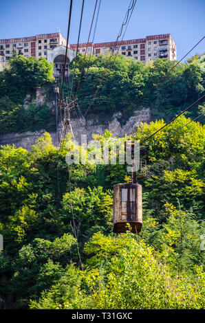 Blick auf eine alte Seilbahn hängen an Seilen von der Talstation mit blauem Himmel und Gebäude auf einem Hügel im Hintergrund. Stockfoto