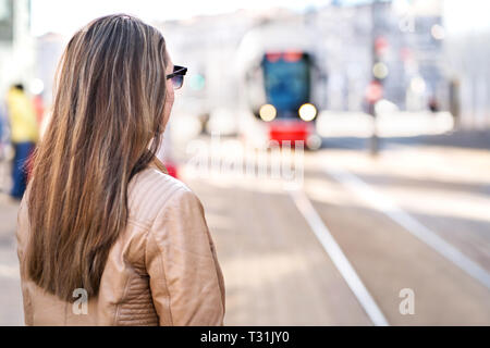 Rückansicht der Frau warten auf die Straßenbahn im Stop. Passagiere, die an der S-Bahn an der Station. Pendler oder Studenten oder mit den öffentlichen Verkehrsmitteln. Stockfoto