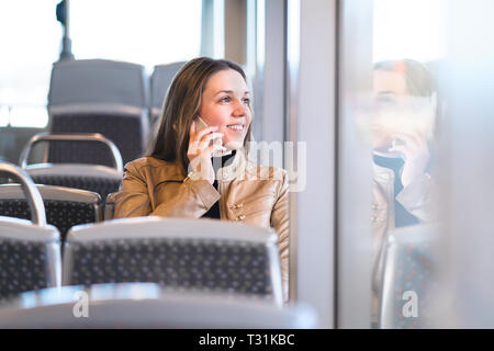 Frau Telefonieren während der Fahrt mit dem Bus, Bahn, U-Bahn oder der U-Bahn. Glückliche Dame mit Smartphone in öffentlichen Verkehrsmitteln Blick aus dem Fenster. Stockfoto