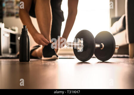 Morgendliche Trainingsroutine im Fitnessstudio. Fitness-Motivation und Muskeltrainings-Konzept. Mann in Turnschuhen, der Schnürsenkel im Sonnenlicht bindet. Stockfoto