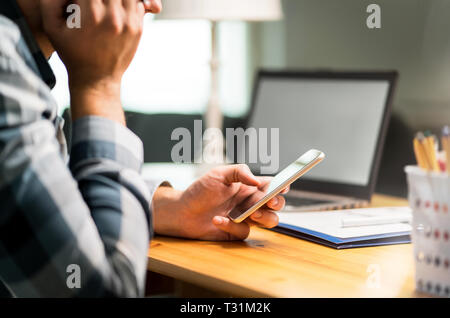 Faule Arbeiter mit Telefon im Büro zu vermeiden. Gelangweilt, traurig oder unzufrieden Mann lehnte sich gegen Hand- und Surfen social media im Internet mit dem Smartphone. Stockfoto