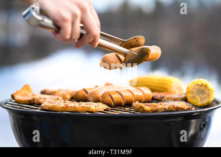 Person grillen mit einem Holzkohlengrill voller köstlicher Speisen. Kochen in der Küche im Freien in der Natur. Mann oder Frau mit Wurst. Stockfoto