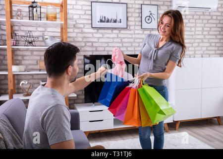 Lächelnde Frau neue Kleidung zu Ihrem Mann sitzen Sofa zu Hause angezeigt Stockfoto