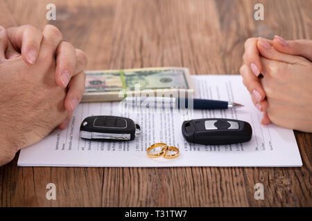 Nahaufnahmen der Hände auf Scheidung Dokument mit Hochzeit Ringe und Autoschlüssel über Holz- Tabelle Stockfoto