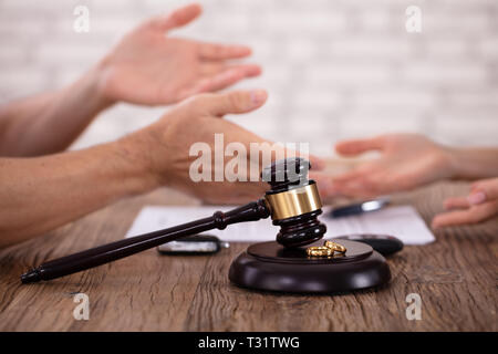 In der Nähe von Paar streiten Miteinander und Schlägel mit goldenen Ringen auf hölzernen Schreibtisch Stockfoto