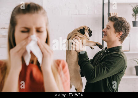 Selektiver Fokus der fröhlichen stattlicher Mann mit niedlichen Mops Hund in der Nähe von Frau Niesen im Gewebe suchen Stockfoto