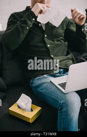 7/8-Ansicht des Menschen mit Allergie und Niesen im Gewebe bei der Verwendung von Laptops Stockfoto