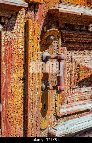 Metall Griff an der alten Holztür, alten grünen mit abblätternder Farbe und rote Schicht unter es gemalt. Vertikale Textur Stockfoto