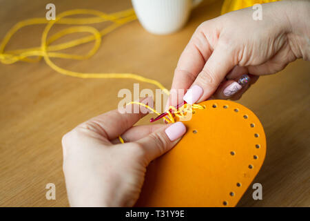 Die Hände der jungen Frau stricken Häkeln von gelb Garn auf hellem Holz- Oberfläche. Eine neue Tasche von Garn zu starten. Selektive Weichzeichner. Stockfoto