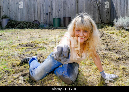 Blonde Frau mittleren Alters mit Schmutz auf Ihrem Gesicht, Arbeiten in Ihrem Garten. Siehe Alamy Bild W3RBAY für daraus resultierende Wildblumen. Stockfoto