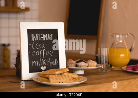 Menü vorstand, Gerichte mit Waffeln und Kuchen und Kanne mit frischem Saft auf der Theke im Coffee Shop Stockfoto