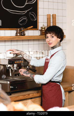 Selektiver Fokus der lächelnden barista Kaffee auf Kaffeemaschine und Kamera Stockfoto