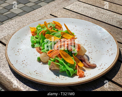 Italienisch bunte Nudeln mit Meeresfrüchten - Jakobsmuschel, Garnelen und Tintenfisch fangarme. Mit Gelben daisy Blüten dekoriert. Schöne und originelle Gerichte Stockfoto